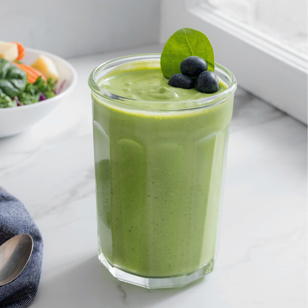 An Arcoroc 21 oz. working glass filled with a green smoothie with a straw.