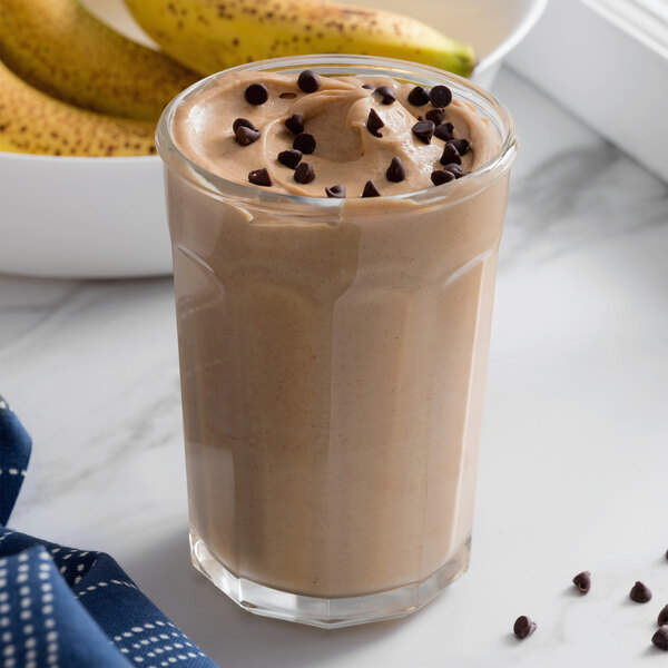 A glass of chocolate milkshake with chocolate chips on a blue tablecloth.