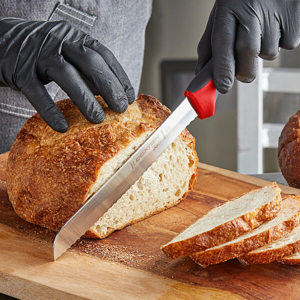 A person in black gloves using a Dexter-Russell scalloped bread knife to cut a loaf of bread.