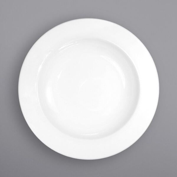 A close-up of an International Tableware white porcelain soup bowl with a wide rim.