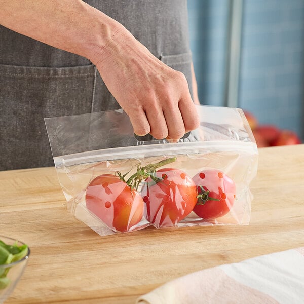 A hand holding a clear plastic bag of tomatoes.