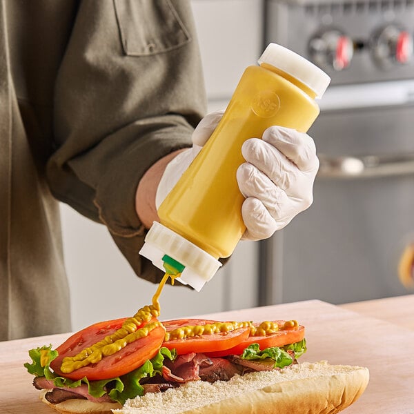 A hand in a glove using a FIFO Innovations clear squeeze bottle with thin dispenser to pour yellow liquid onto a sandwich.