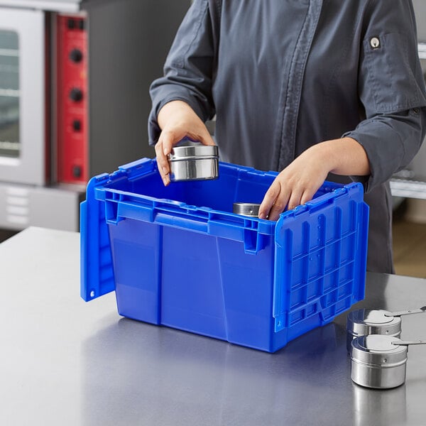 A woman in a chef's uniform holding a dark blue Orbis Stack-N-Nest Flipak tote box with hinged lid.