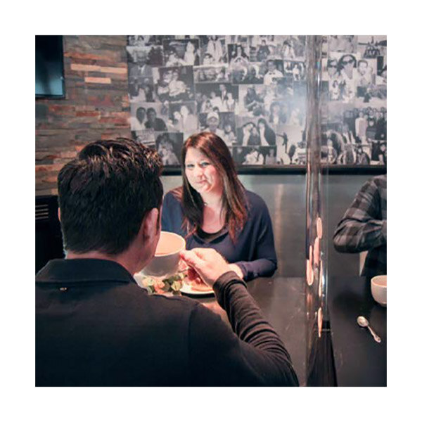 An American Metalcraft clear PVC restaurant partition on a table in a farm-to-table restaurant with a man and woman sitting at a table.