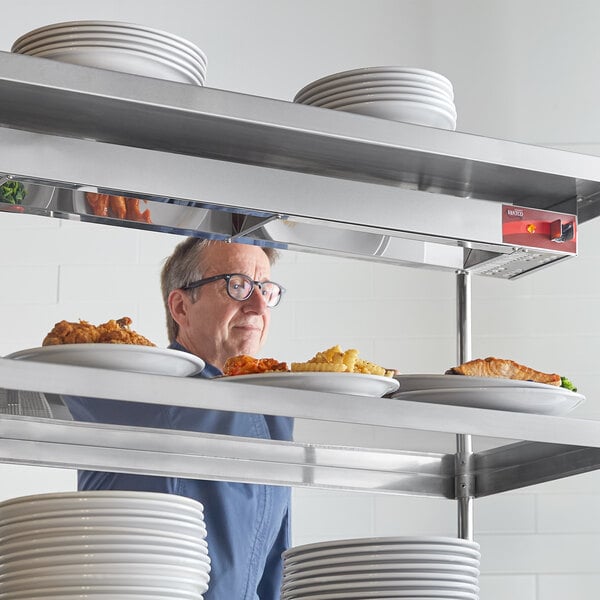 A man standing behind a shelf with plates of food using an Avantco strip warmer.