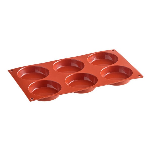 A red silicone baking pan with six flan-shaped cavities.