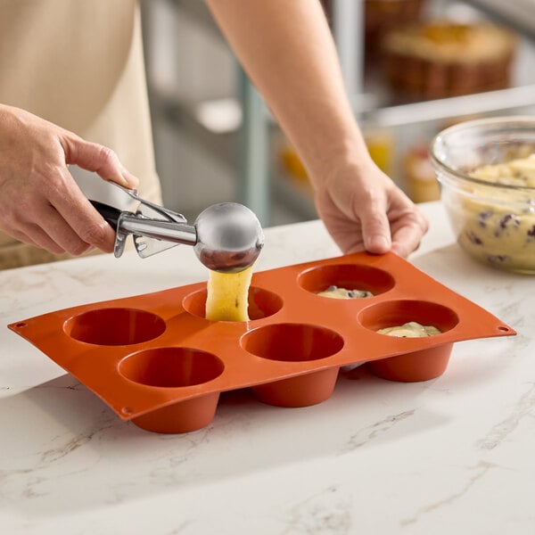 A red silicone baking mold with six medium muffin compartments being filled with batter.