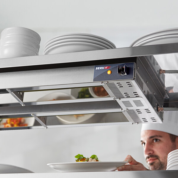 A chef using a ServIt double strip warmer to heat a plate of food in a professional kitchen.