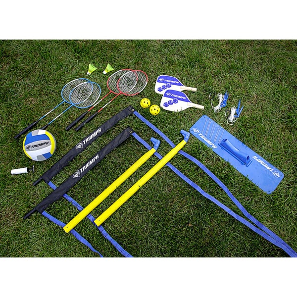 A Triumph multi-sport net set with badminton rackets and a volleyball on grass.