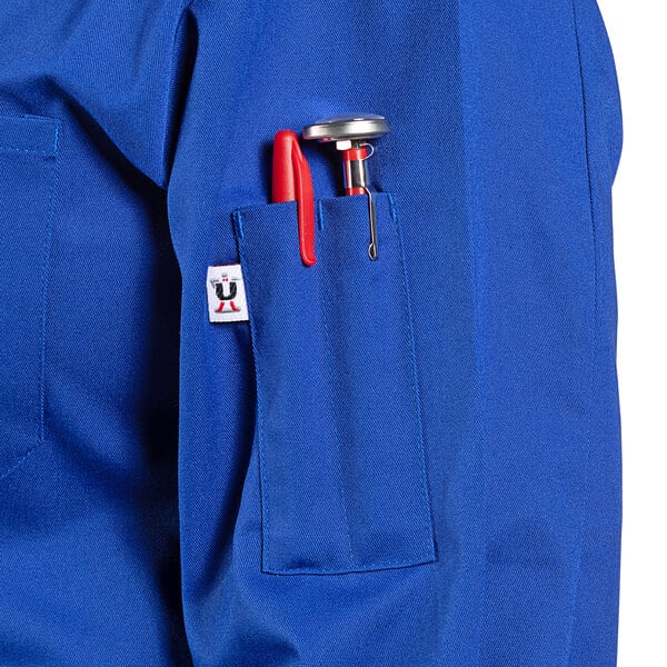 A royal blue Uncommon Chef long sleeve chef coat with a red pen and pen holder in the pocket.