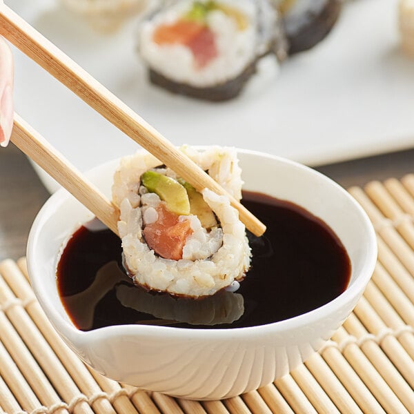 A hand holding chopsticks to a sushi roll dipped in Lee Kum Kee soy sauce.