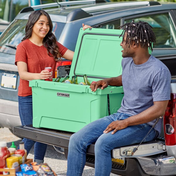 A man and woman sitting on the back of a truck with a CaterGator seafoam cooler.