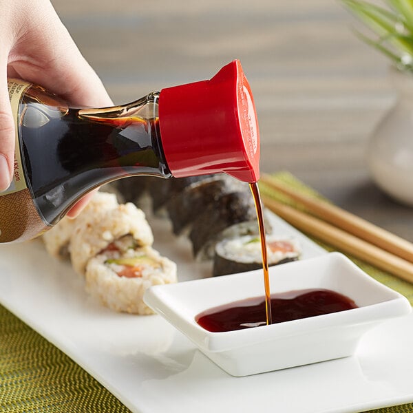 A hand pouring Lee Kum Kee soy sauce into a bowl of sushi.