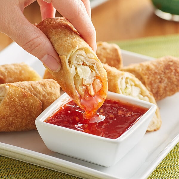 A person dipping a fried egg roll into a bowl of Lee Kum Kee Thai Sweet Chili Sauce.