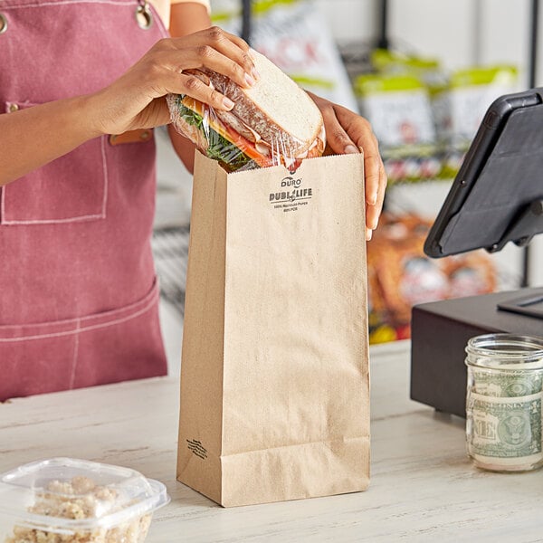 A woman holding a sandwich in a Duro brown paper bag.