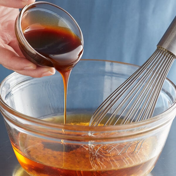 A hand pouring Lee Kum Kee oyster flavored sauce into a glass bowl of liquid.