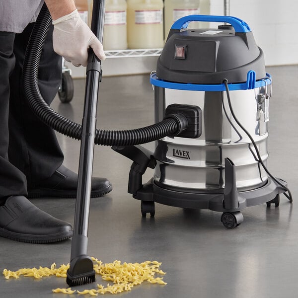 A person using a Lavex stainless steel wet/dry vacuum to clean the floor in a professional kitchen.