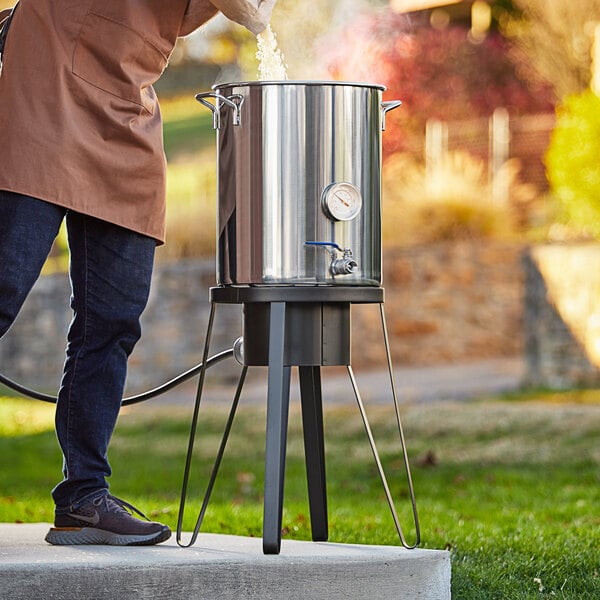 A man pouring water into a large stainless steel pot on a gas stove stand.