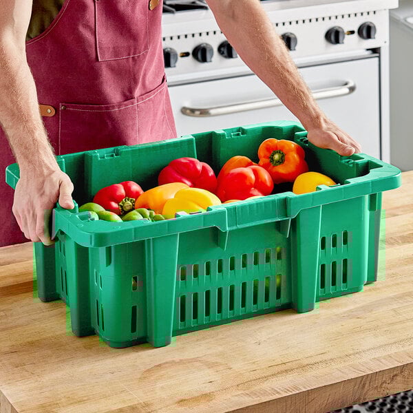 A man in an apron holding a green Orbis agricultural crate full of vegetables.