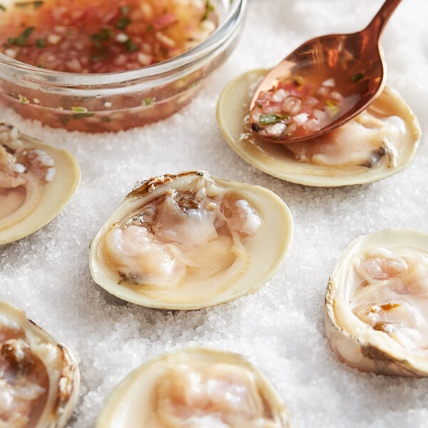 A group of Rappahannock Oyster Co. Olde Salt middleneck clams on a white surface with a spoon and a bowl of sauce.