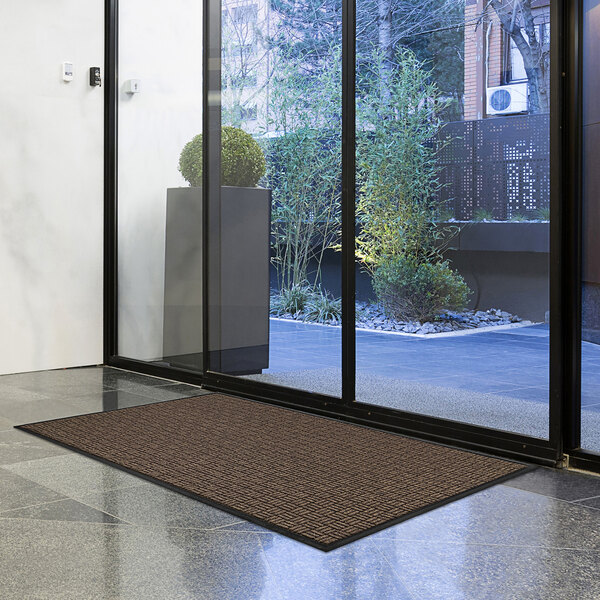 A brown Lavex parquet entrance mat on the floor in front of a glass door.