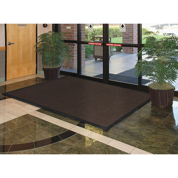 A large brown Lavex carpet mat in front of a glass door.