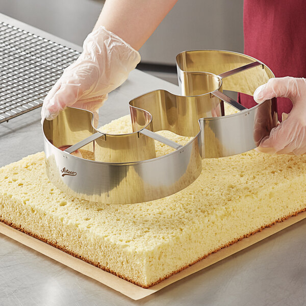 A gloved hand using an Ateco stainless steel number 3 cutter to cut a cookie.