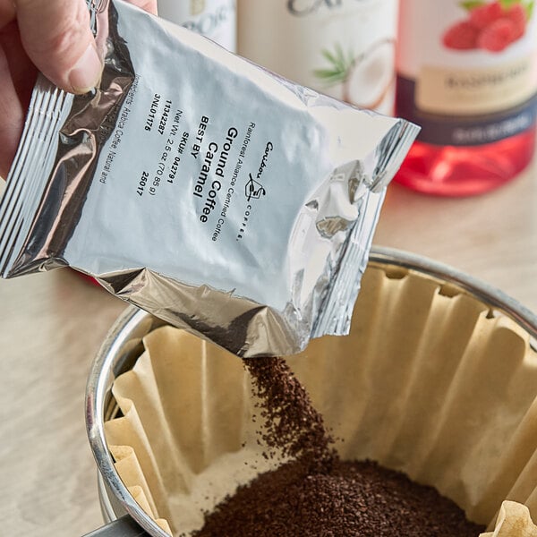 A hand pouring Caribou Coffee ground coffee into a filter.