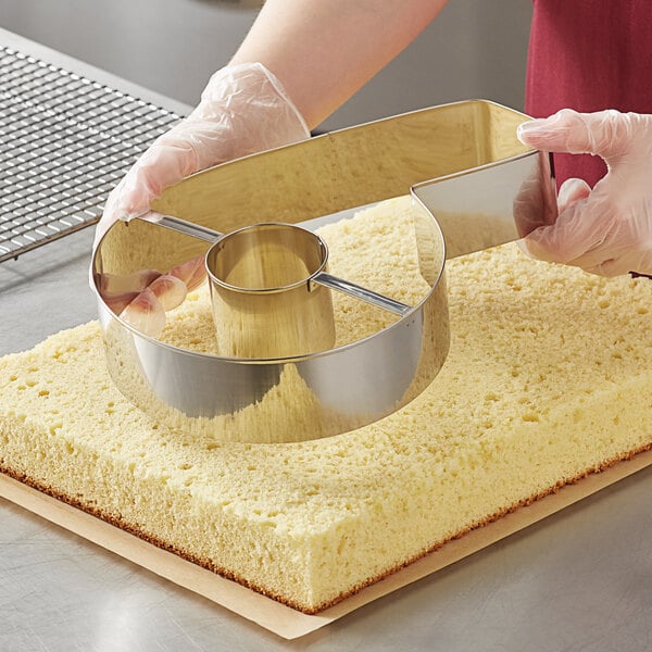 A person using an Ateco stainless steel number cutter to cut a cake.