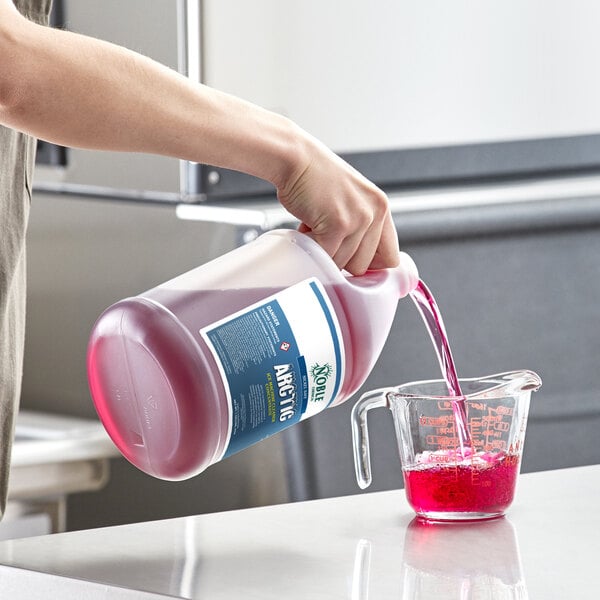 A person pouring Noble Chemical Arctic concentrated liquid into a measuring cup on a counter in a professional kitchen.