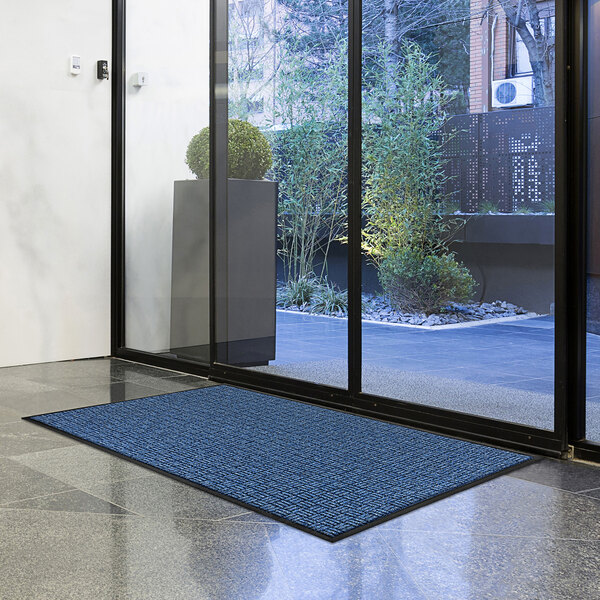 A navy blue Lavex parquet entrance mat on the floor in front of a glass door.