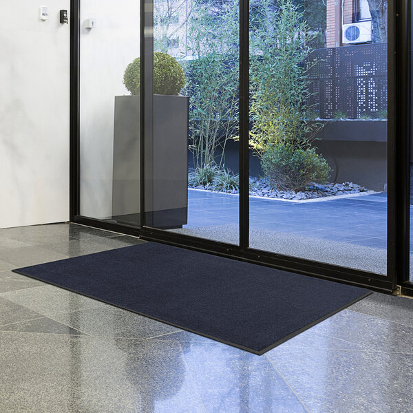 A navy blue Lavex doormat on the floor in front of a glass door.