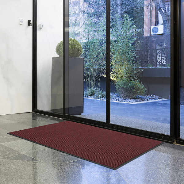 A red Lavex Needle Rib entrance mat unrolled in front of a glass door.