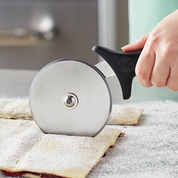 A person using an Ateco stainless steel pastry cutter with a black polypropylene handle to cut pastry.