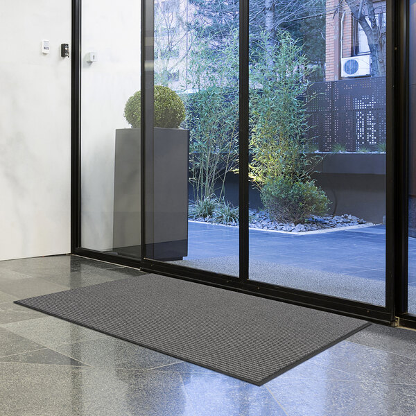 A large gray Lavex Needle Rib indoor entrance mat in front of a glass door.