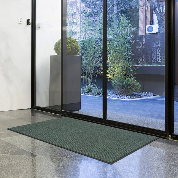 A green Lavex Needle Rib entrance mat on the floor in front of a glass door.