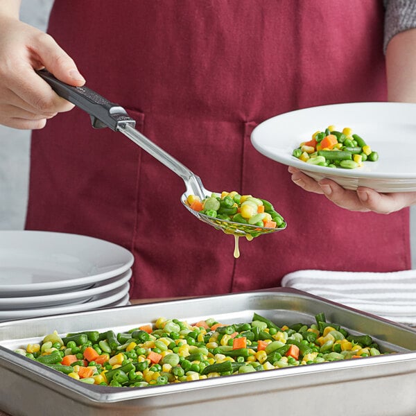 A person using a Vollrath slotted spoon to serve vegetables onto a plate.