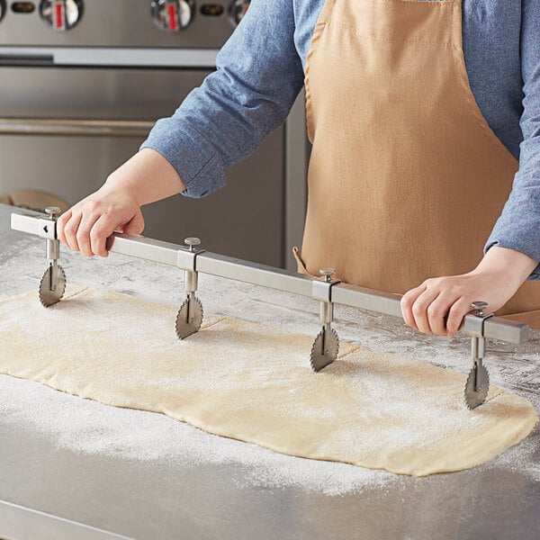 A person in a professional kitchen using an Ateco stainless steel multi-wheel pastry cutter to cut dough.