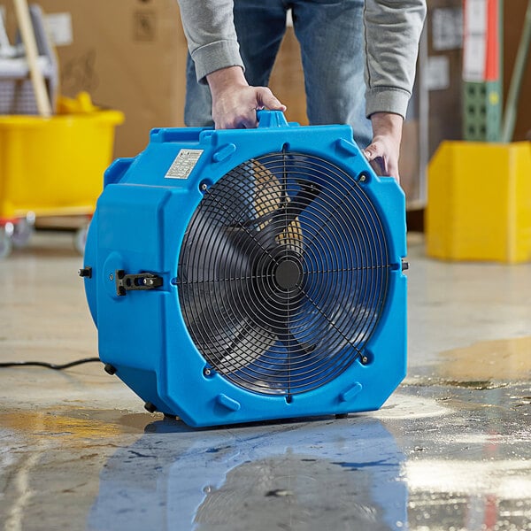 A man holding a blue Lavex industrial axial fan with black accents.