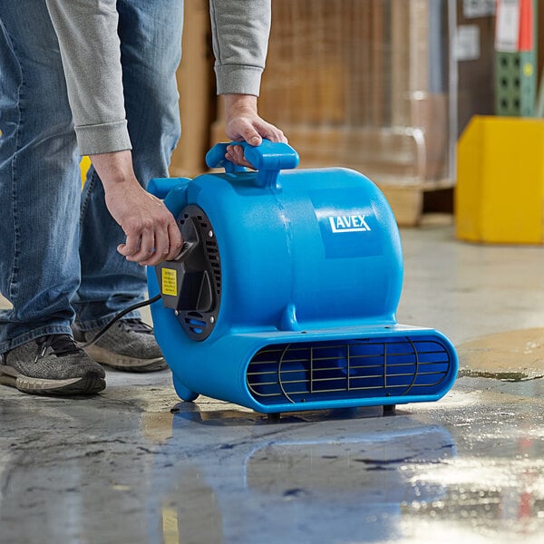 A man using a Lavex blue compact air mover to dry a floor.