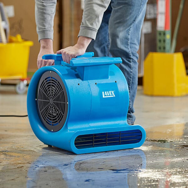 A man using a Lavex blue commercial air mover to clean the floor in a grocery store aisle.