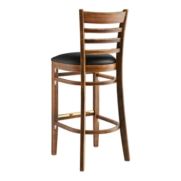 A Lancaster Table & Seating wood ladder back bar stool with black vinyl seat.