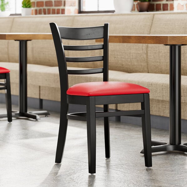 A Lancaster Table & Seating Black Wood Ladder Back Chair with Red Vinyl Seat on a black chair with a red cushion