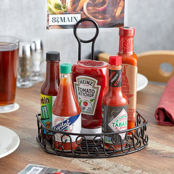 An American Metalcraft wrought iron condiment caddy holding a ketchup and hot sauce bottle on a table.