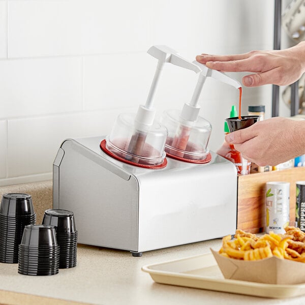 A person pouring red liquid into a Steril-Sil stainless steel condiment dispenser.