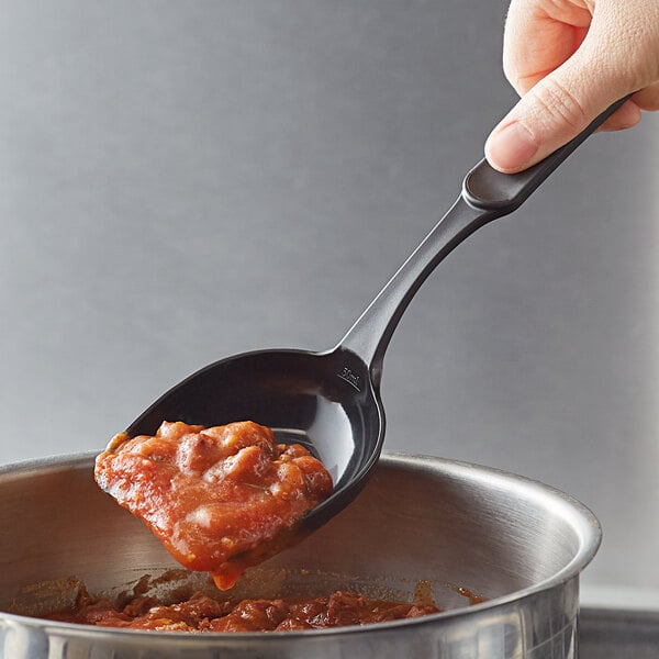 A person holding a Linden Sweden black high-heat nylon prep spoon full of food over a bowl.
