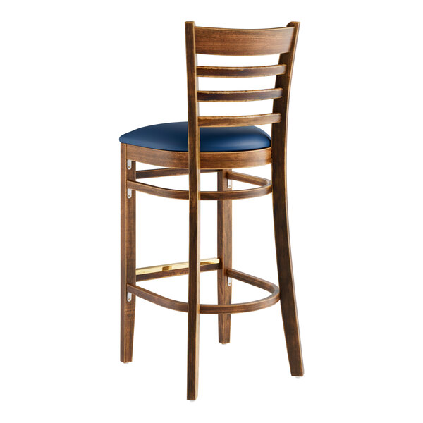 A Lancaster Table & Seating wooden bar stool with navy blue cushion.