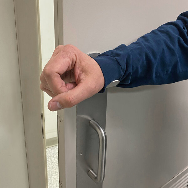 A person's hand using a Nemco Clean Getaway stainless steel door opener to hold a metal door handle.