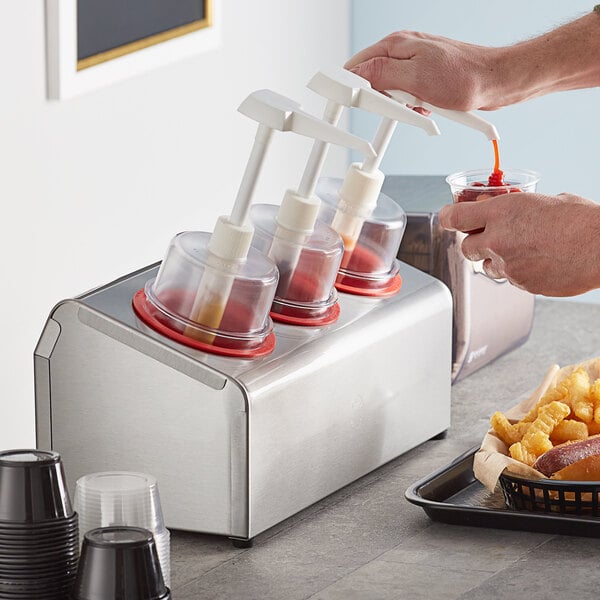 A person pouring ketchup into a white Steril-Sil condiment dispenser with red pump tops.