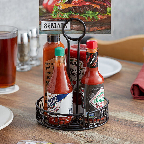 A group of hot sauces in a black metal holder on a table.